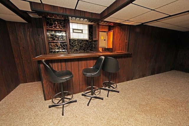 bar with wooden walls, carpet flooring, and a drop ceiling