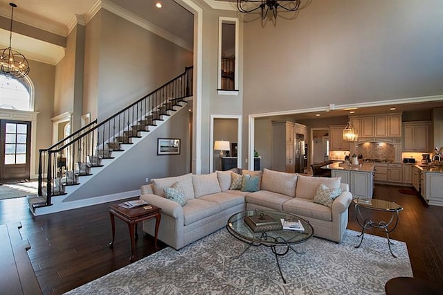 living room featuring dark hardwood / wood-style floors, crown molding, a towering ceiling, and an inviting chandelier