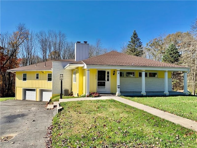 ranch-style home featuring central AC unit, covered porch, a front lawn, and a garage