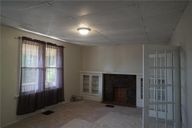 unfurnished living room featuring light colored carpet, a drop ceiling, and a wealth of natural light