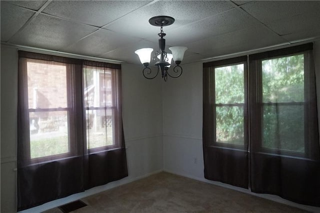 carpeted empty room featuring a paneled ceiling, a notable chandelier, and a healthy amount of sunlight