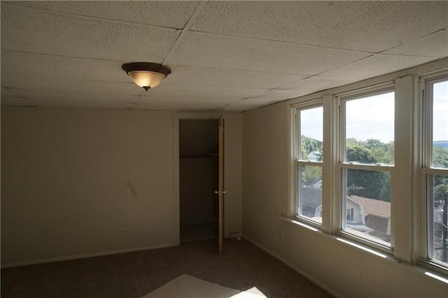 unfurnished bedroom with carpet flooring, multiple windows, and a drop ceiling