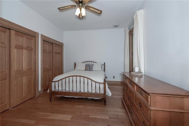 bedroom featuring ceiling fan, two closets, and light hardwood / wood-style flooring