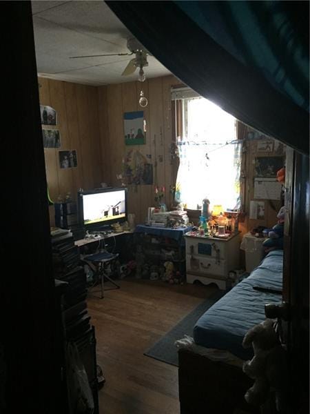 bedroom with wood walls, ceiling fan, and dark wood-type flooring