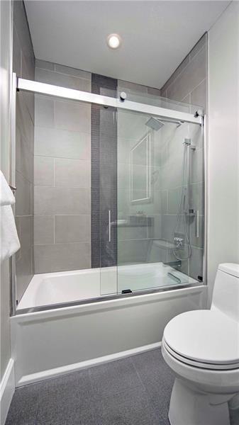 bathroom featuring toilet, combined bath / shower with glass door, and tile floors