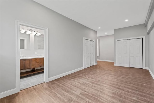 unfurnished bedroom featuring two closets, ensuite bath, and hardwood / wood-style floors