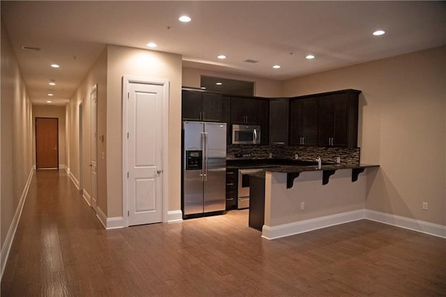 kitchen featuring appliances with stainless steel finishes, tasteful backsplash, kitchen peninsula, light wood-type flooring, and a kitchen breakfast bar