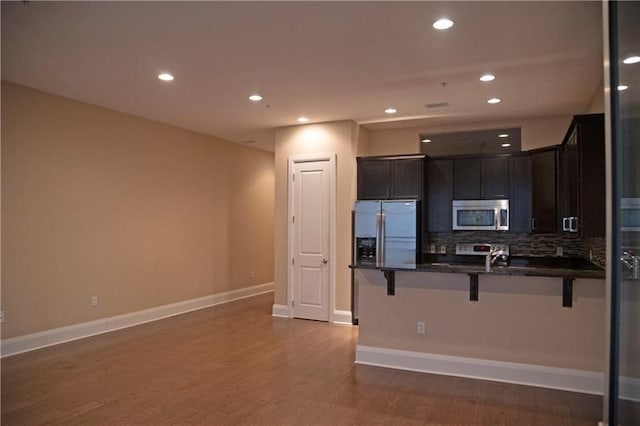 kitchen featuring a kitchen bar, backsplash, wood-type flooring, and stainless steel appliances