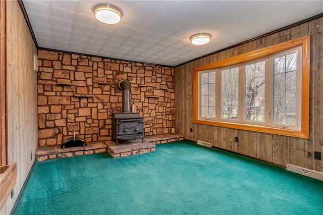 interior space with a wood stove, dark carpet, and wood walls