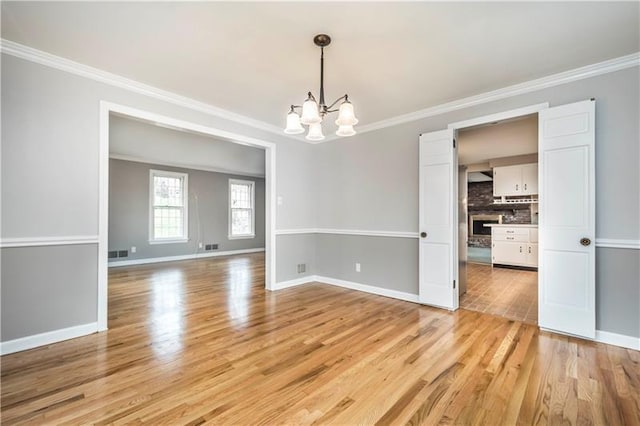 empty room with a notable chandelier, crown molding, and light hardwood / wood-style floors