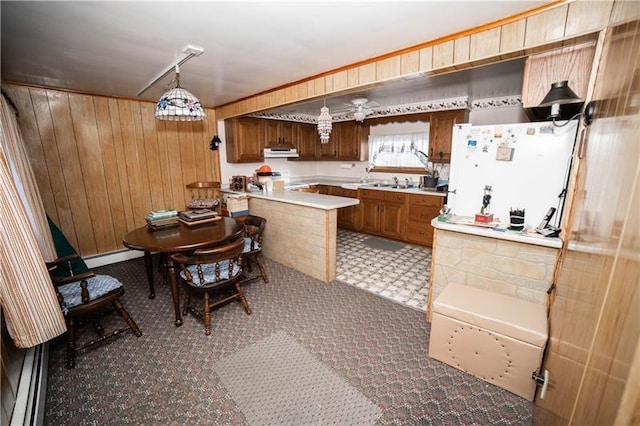 kitchen featuring pendant lighting, wooden walls, a baseboard radiator, white refrigerator, and kitchen peninsula