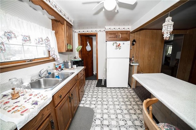 kitchen with sink, white fridge, hanging light fixtures, light tile flooring, and ceiling fan with notable chandelier