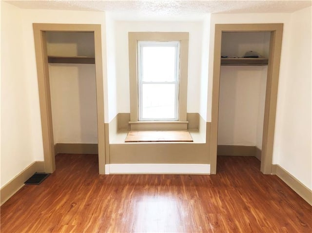 unfurnished bedroom featuring dark hardwood / wood-style floors, multiple closets, and a textured ceiling