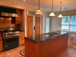 kitchen with sink, high end range, wall chimney exhaust hood, backsplash, and hanging light fixtures