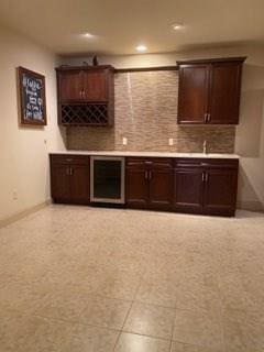 bar featuring wine cooler, dark brown cabinets, tasteful backsplash, and light tile floors