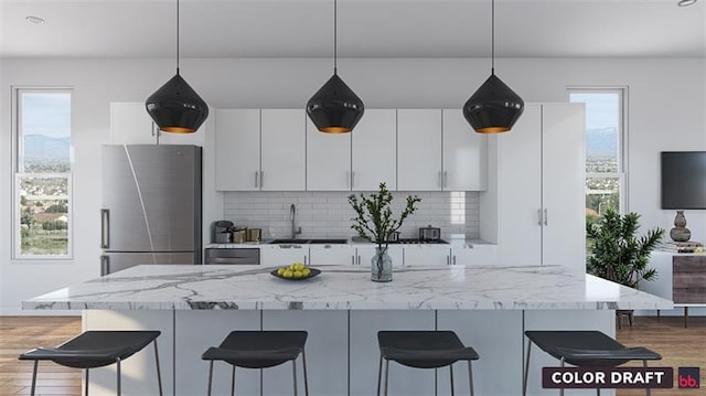 kitchen featuring pendant lighting, stainless steel refrigerator, light hardwood / wood-style flooring, light stone countertops, and white cabinets