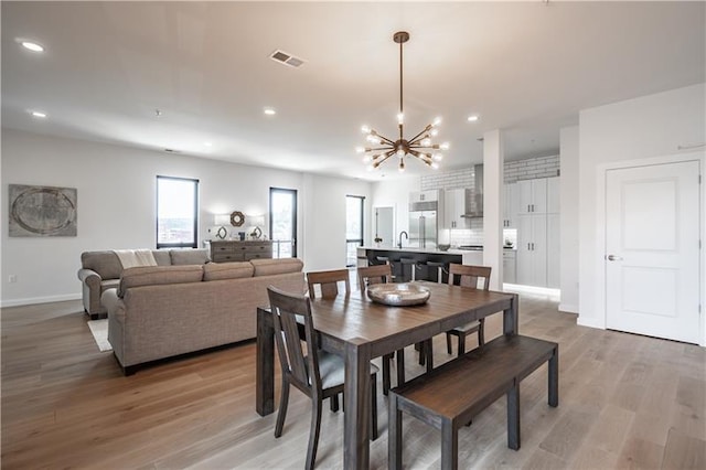 dining space with a notable chandelier, sink, and light hardwood / wood-style flooring