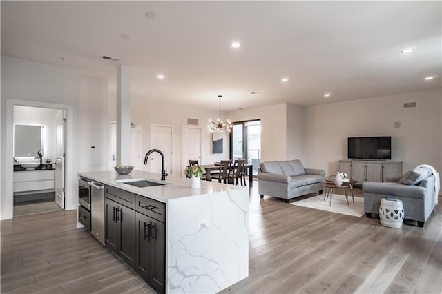 kitchen with an inviting chandelier, stainless steel dishwasher, sink, hardwood / wood-style flooring, and a center island with sink