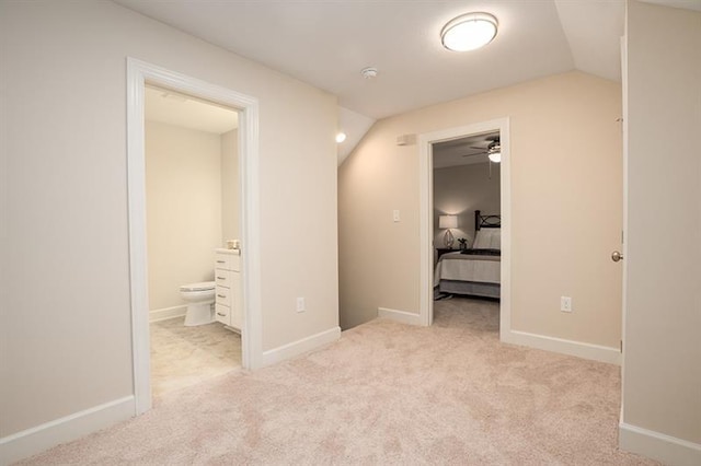 unfurnished bedroom with ensuite bath, light colored carpet, and vaulted ceiling