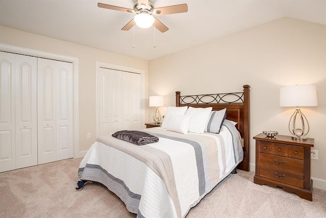 bedroom featuring light carpet, lofted ceiling, ceiling fan, and multiple closets