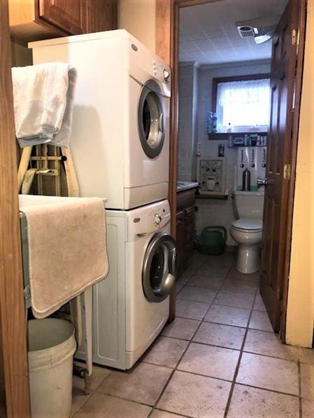 laundry room featuring stacked washer and dryer and light tile floors