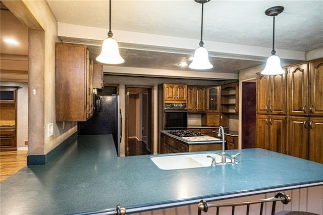 kitchen featuring pendant lighting, hardwood / wood-style floors, black appliances, a textured ceiling, and sink