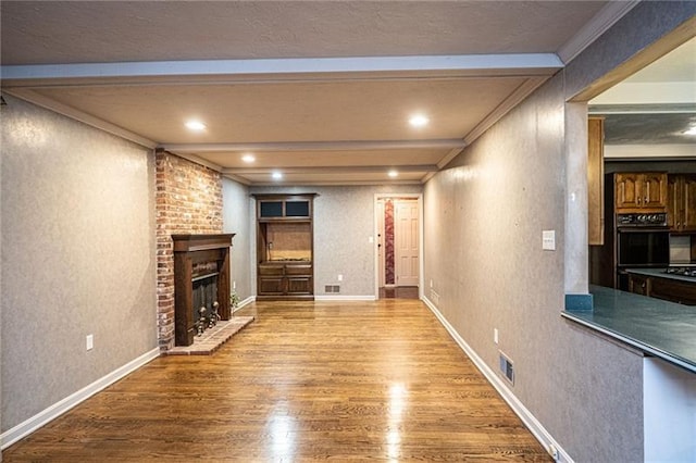 unfurnished living room featuring crown molding, hardwood / wood-style floors, a brick fireplace, and beamed ceiling