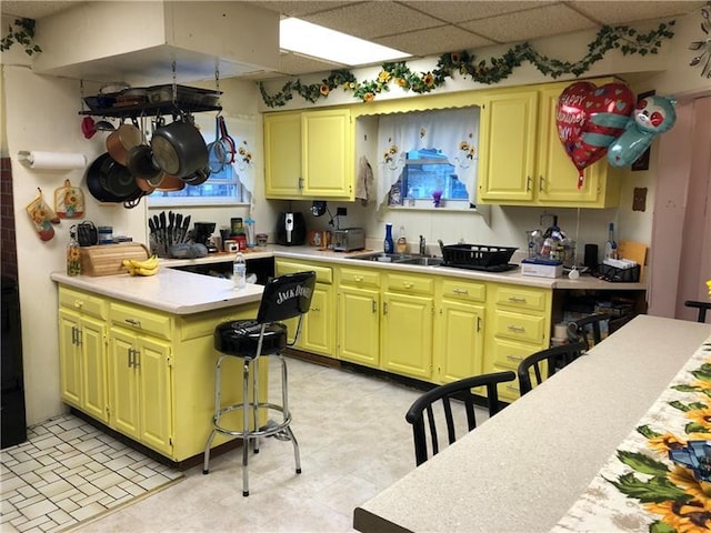 kitchen with a paneled ceiling, a breakfast bar, sink, and light tile flooring