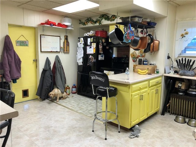 kitchen with black fridge, a drop ceiling, light tile floors, and range