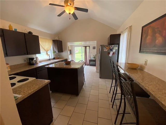 kitchen featuring light tile flooring, stainless steel refrigerator, lofted ceiling, ceiling fan, and a kitchen breakfast bar