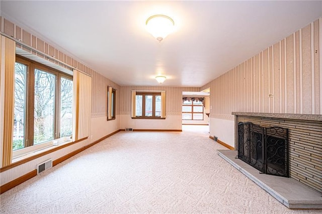 unfurnished living room with light carpet, wood walls, and a wealth of natural light