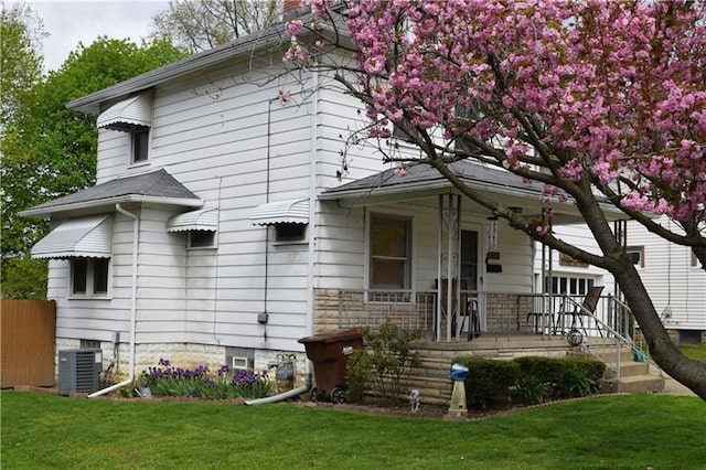 rear view of house with covered porch, central AC, and a yard