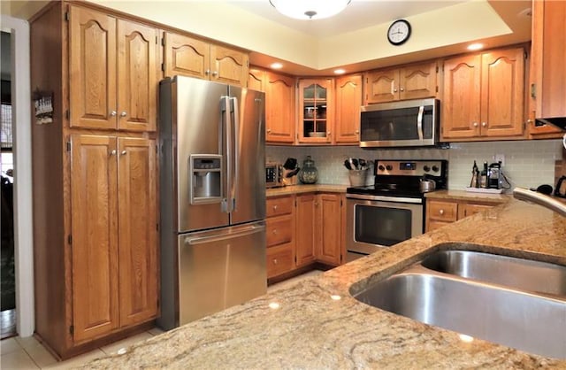 kitchen featuring backsplash, appliances with stainless steel finishes, light stone countertops, and sink