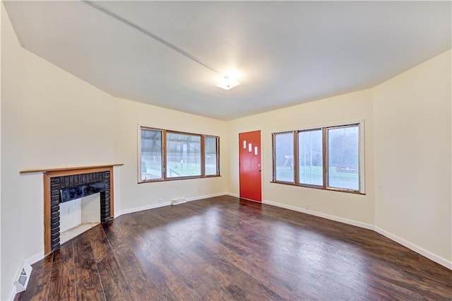 unfurnished living room featuring dark wood-type flooring, a brick fireplace, and a healthy amount of sunlight