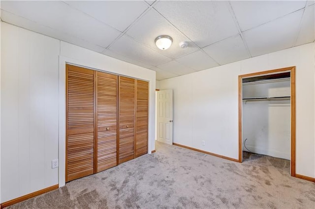 unfurnished bedroom with a paneled ceiling, a closet, and light carpet