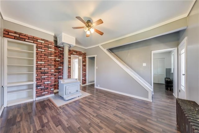 unfurnished living room featuring dark wood-type flooring, ornamental molding, ceiling fan, and a wood stove