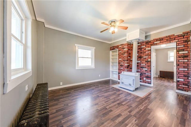 unfurnished living room featuring dark wood-type flooring, radiator heating unit, ceiling fan, and a wood stove