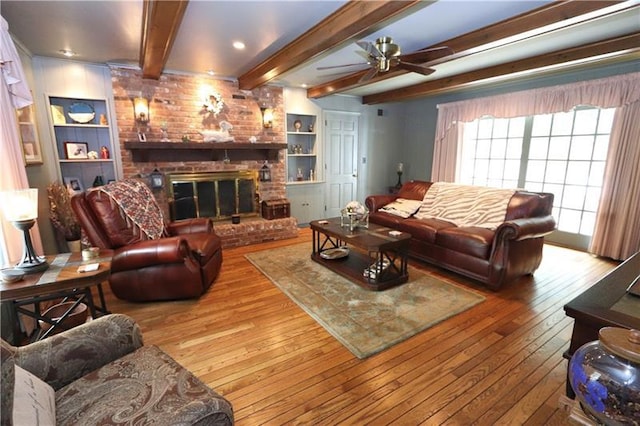 living room featuring beamed ceiling, a fireplace, ceiling fan, and light hardwood / wood-style flooring