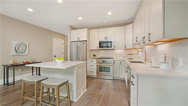 kitchen featuring high quality appliances, white cabinets, light wood-type flooring, backsplash, and a kitchen breakfast bar