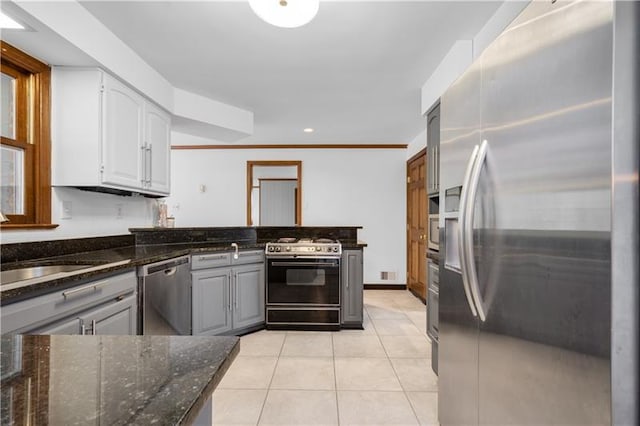 kitchen with ornamental molding, appliances with stainless steel finishes, light tile flooring, and dark stone countertops