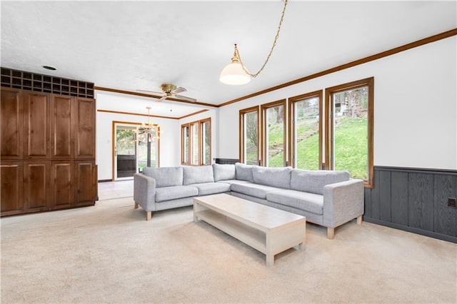 carpeted living room with ornamental molding and ceiling fan with notable chandelier