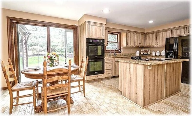 kitchen with light stone countertops, a kitchen island, black appliances, and sink