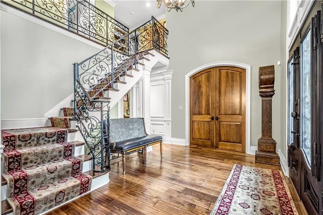 foyer featuring an inviting chandelier, a high ceiling, wood-type flooring, and crown molding