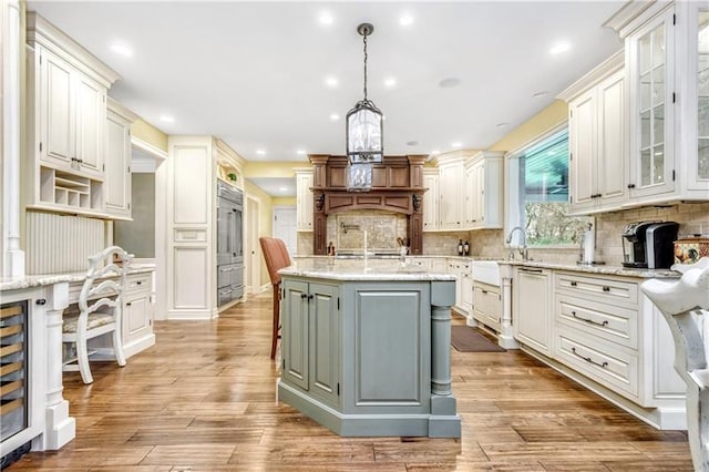 kitchen with light stone counters, an island with sink, light wood-type flooring, backsplash, and hanging light fixtures