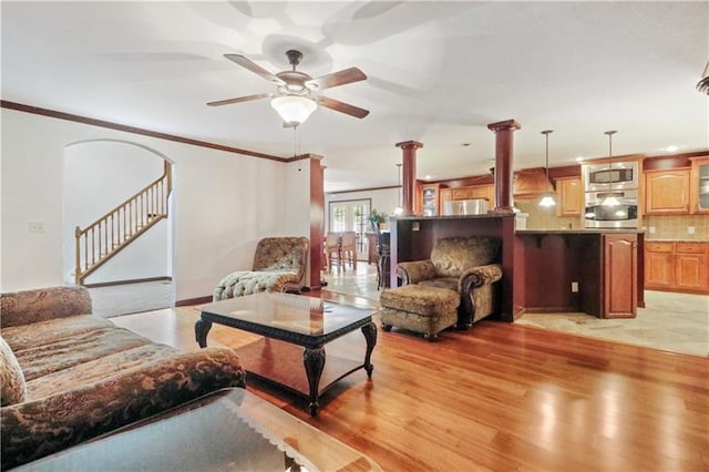 living room featuring light wood-type flooring, ceiling fan, decorative columns, and ornamental molding