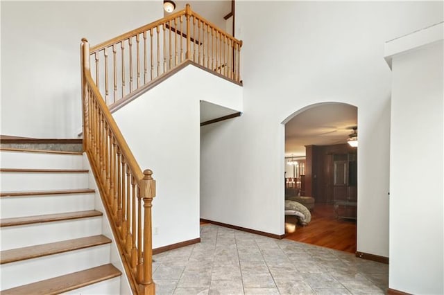 stairway with ceiling fan with notable chandelier, light tile floors, and a towering ceiling