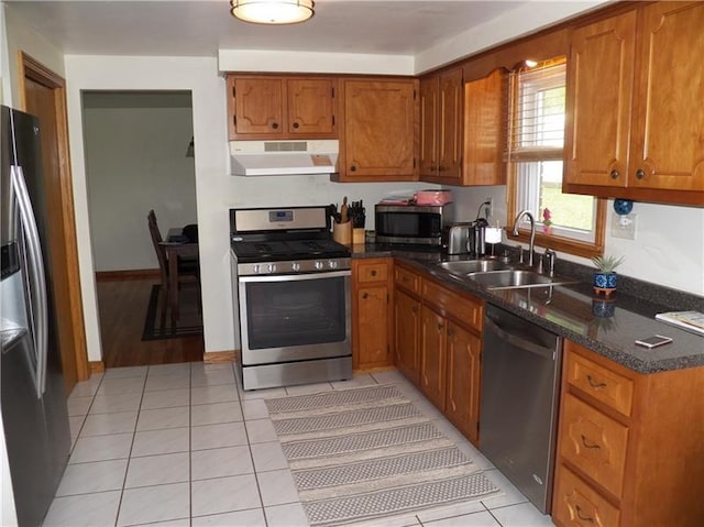 kitchen featuring light tile flooring, range hood, sink, stainless steel appliances, and dark stone countertops