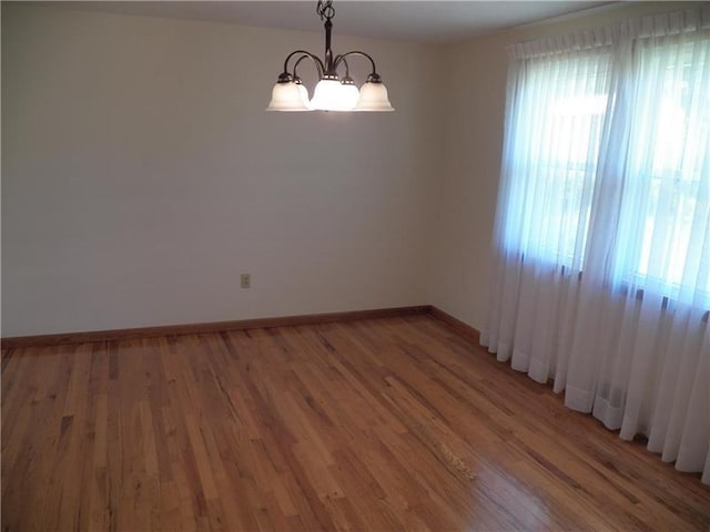 spare room featuring plenty of natural light, an inviting chandelier, and dark wood-type flooring