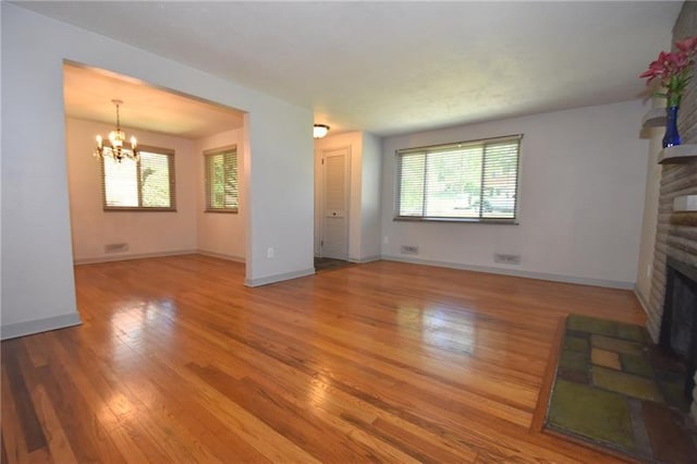 unfurnished living room featuring plenty of natural light, a brick fireplace, light hardwood / wood-style floors, and a notable chandelier