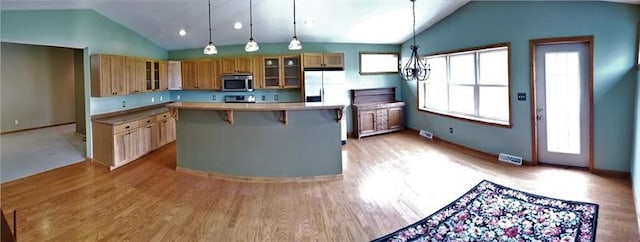 kitchen with appliances with stainless steel finishes, light hardwood / wood-style floors, a kitchen bar, a center island, and pendant lighting